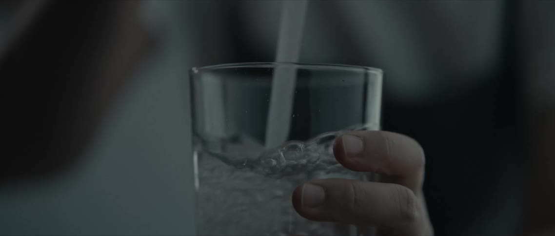 A glass cup being filled from a tap held by a person
