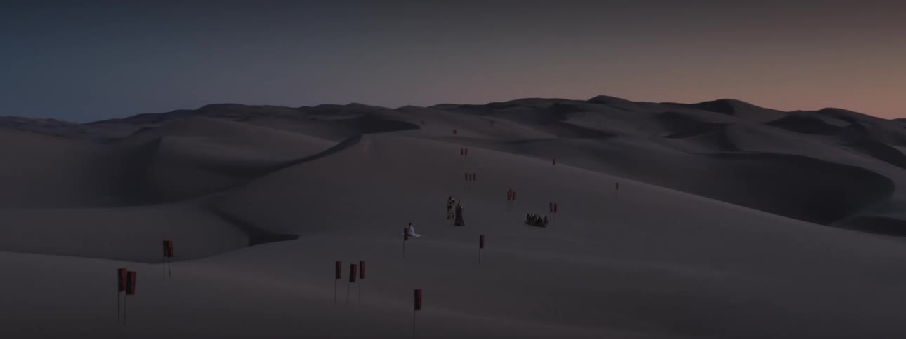 Aerial scenery of desert dunes with flags of a kingdom and three people in the background at dusk