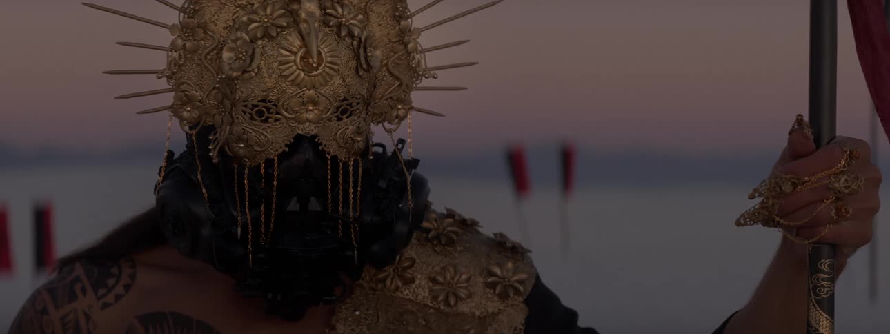 A person with golden accessories and a golden helmet looking straight ahead