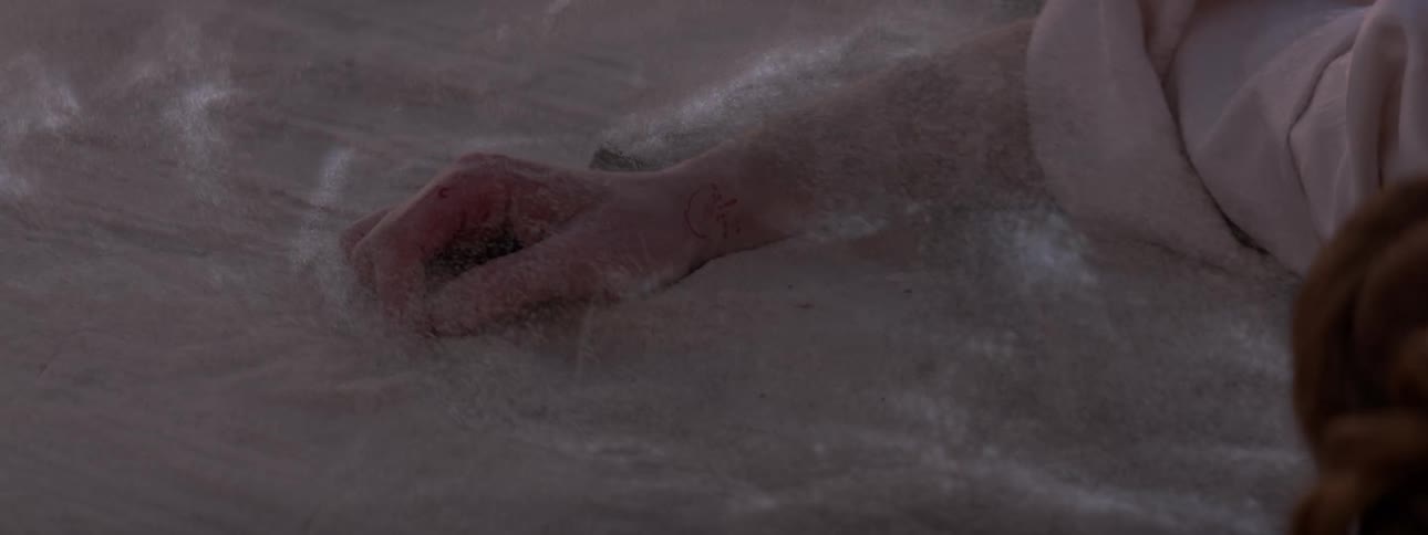 The arm of a person who is lying on the ground and there is sand moving on the surface of the ground and there is a red mark on the persons wrist shining