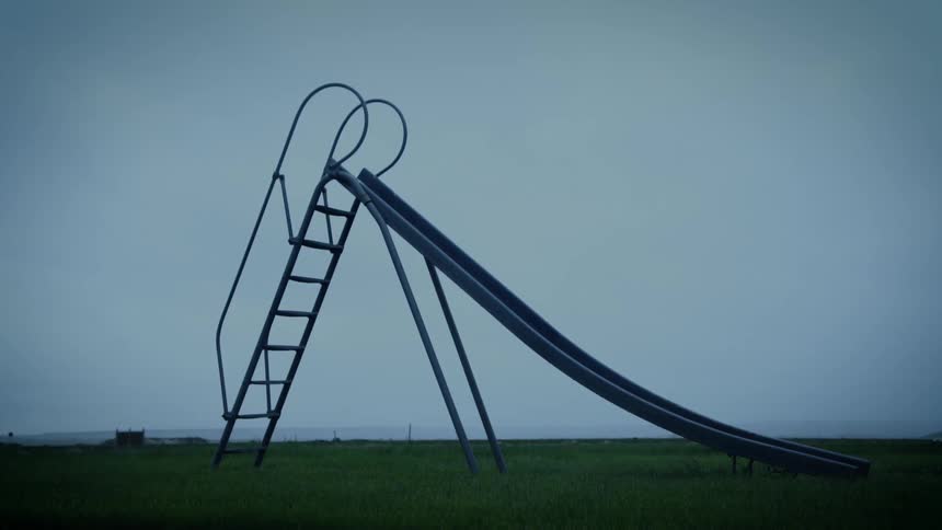 Metal slide with a ladder located in an open field with grass and cloudy sky
