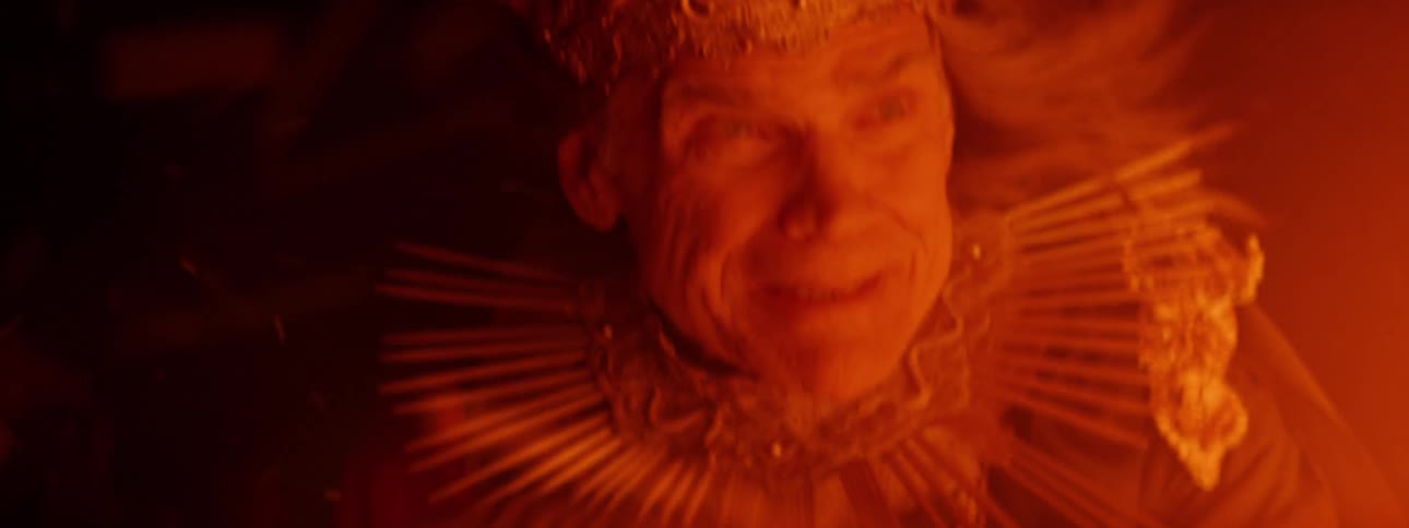 Close up of the face of an elderly man wearing a crown scared looking at flames or fire