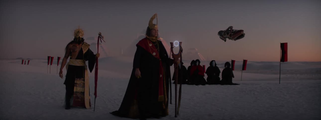 Man with a staff walking through the desert dunes with people kneeling in the background and pyramids and a futuristic spaceship around