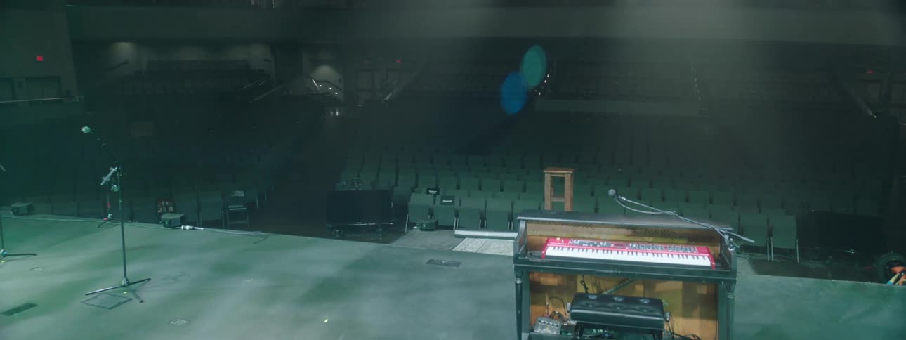 A stage with several empty black chairs and a piano with a microphone on top of the stage