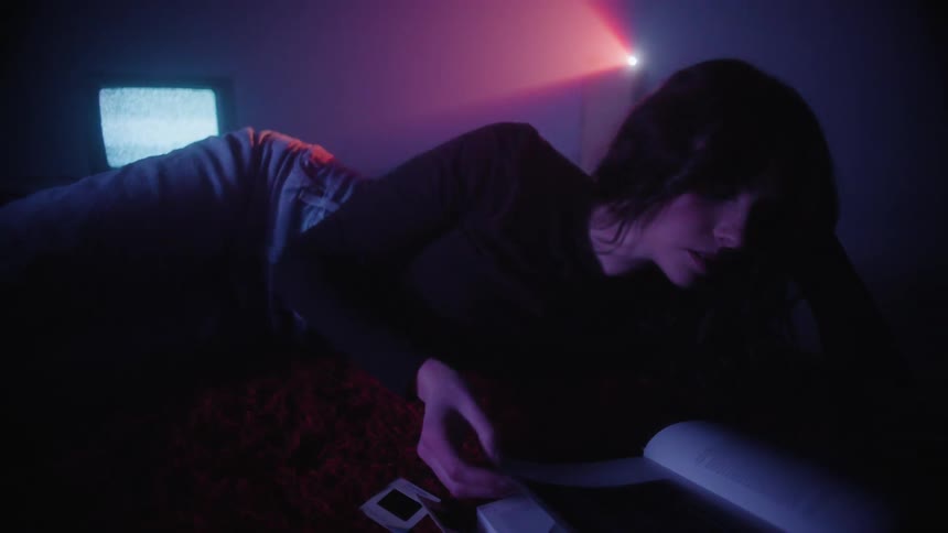 Woman lying on the red carpet reading a book in a dark room with a neon light in the background