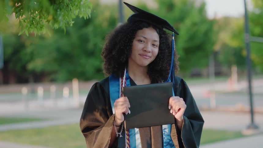 Young smiling woman holding diploma and wearing a graduation cap