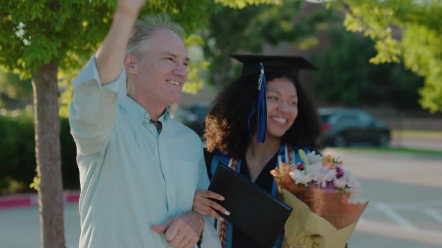 A young woman wearing a graduation cap and gown celebrating outdoors