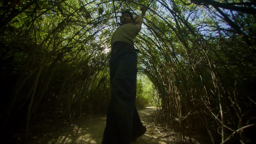 Man dancing in a natural arch of branches and with trees around