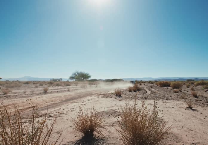 Car accelerating and we make dust fly in a desert terrain on a day with cloudless blue skies and the sun