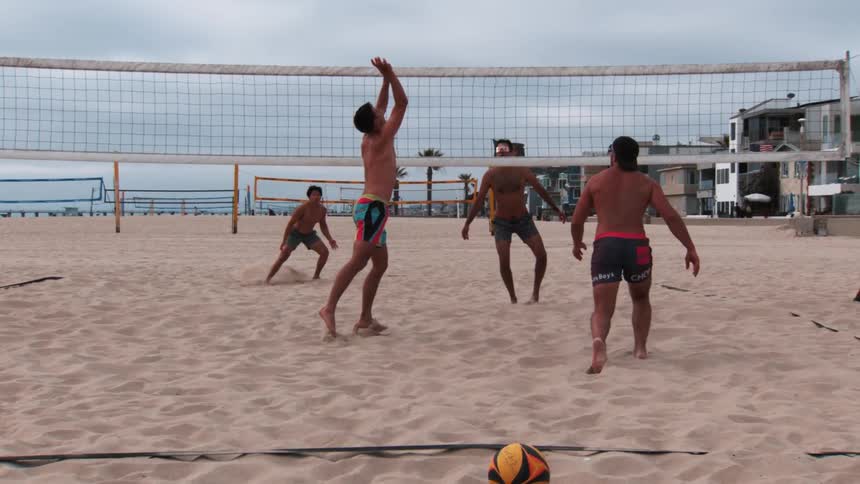 Two pairs of men playing volleyball on the beach sand