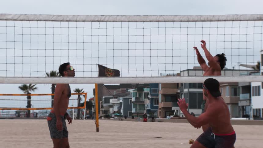 A group of men play volleyball together on the beach