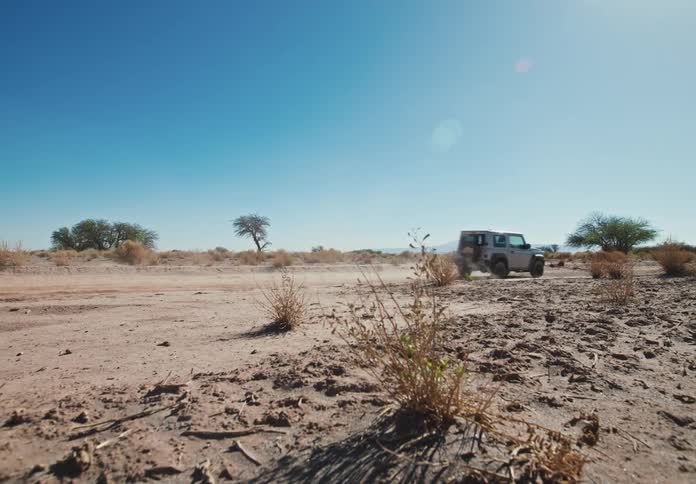 Offroad vehicle kicking up dust in a desert terrain under a clear sky
