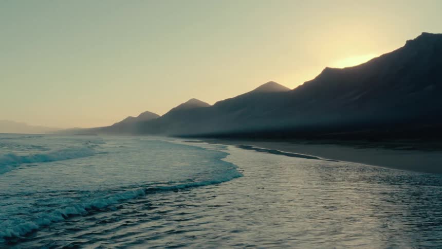 Landscape at dawn with the sun low in the sky softly illuminating mountains by the beach