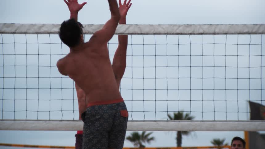 Two men jump towards the net while playing volleyball