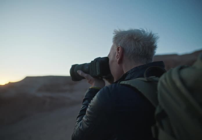 Man holding and looking through a photo camera capturing the beauty of twilight over the mountains
