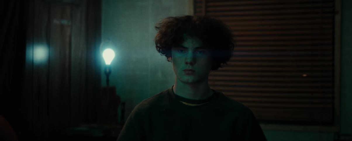 Portrait of a young man sitting in a dark room with a light bulb on in the background