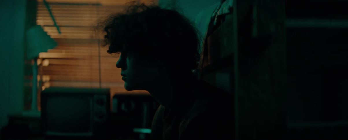 Young man with curly hair sitting indoors with low lighting