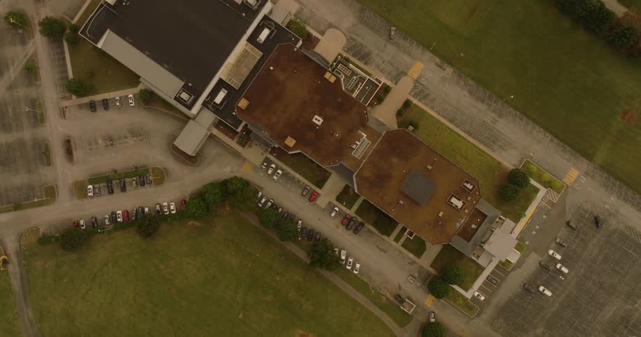 An aerial view of a large building complex with a brown roof surrounded by parking lots and green spaces