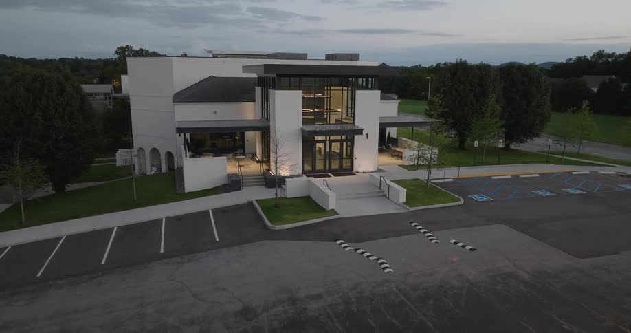 Modern twostory building at dusk with internal lighting on and empty parking lot in front