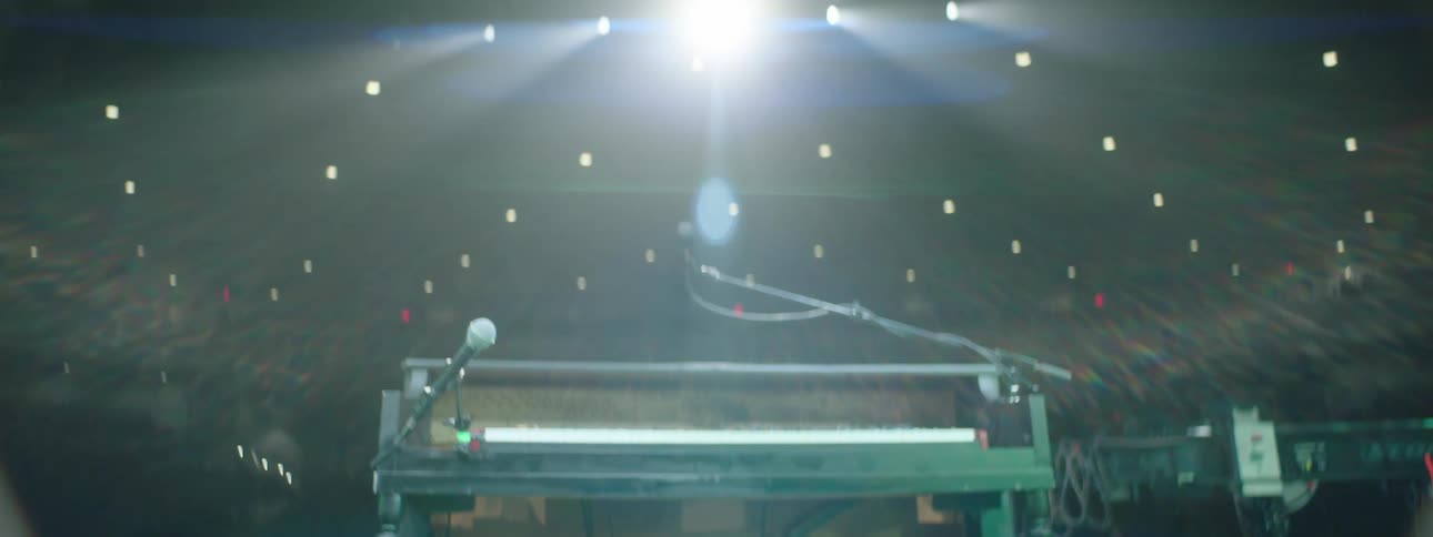 A piano on a stage spotlighted by stage lights with an empty auditorium in the background