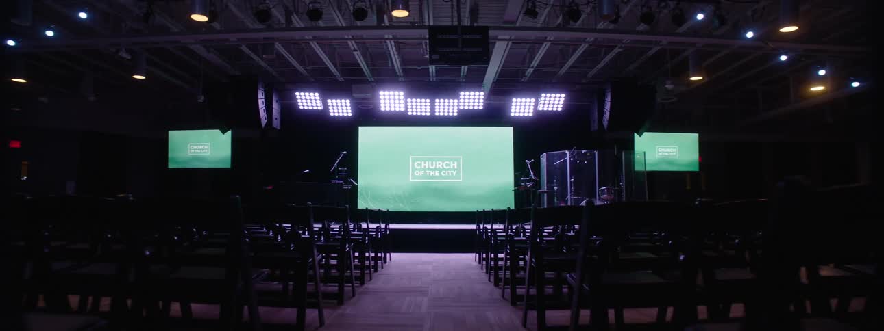 Interior of a dimly lit room in an auditorium with a lit stage and a screen