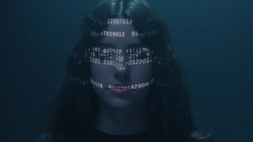 Close up of the head of a young woman with changing numbers projected over her face inside a dimly lit room