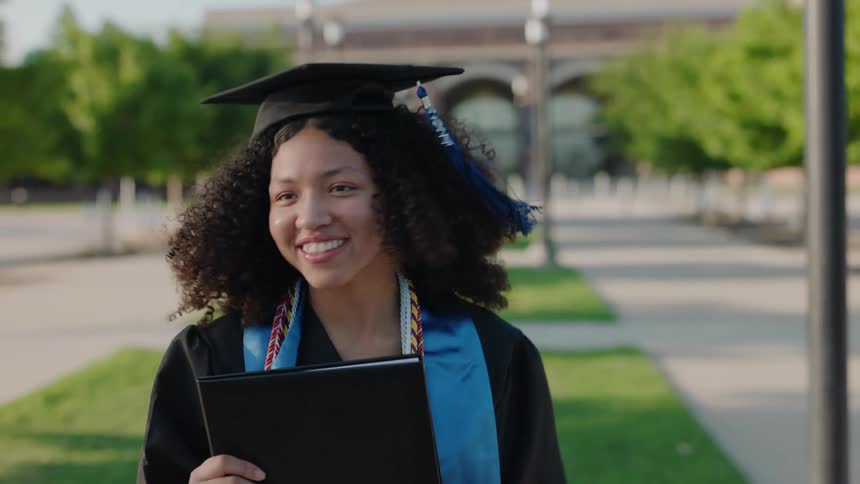 Young curlyhaired woman holding a book while wearing a graduation cap