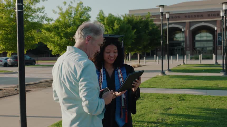 Elderly man talking to a young graduate who is happy and wearing a cap