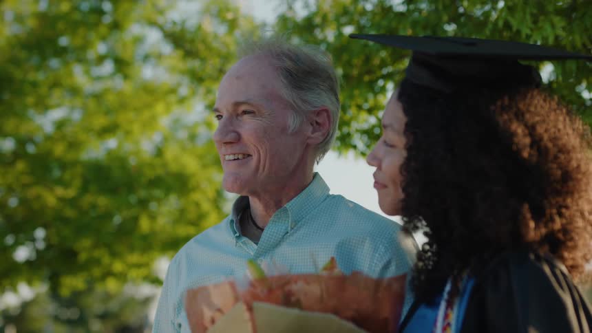 An elderly man next to a young woman who is in graduation clothes and they are happy