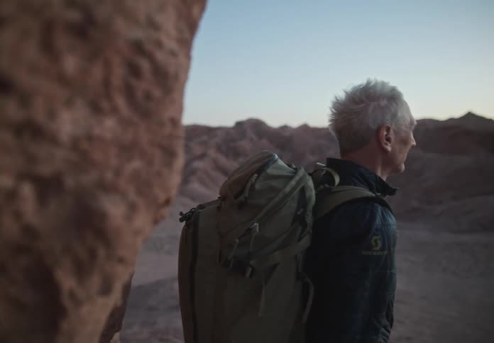 Photographer man holding his professional camera and a backpack on his back in an environment with desert mountains