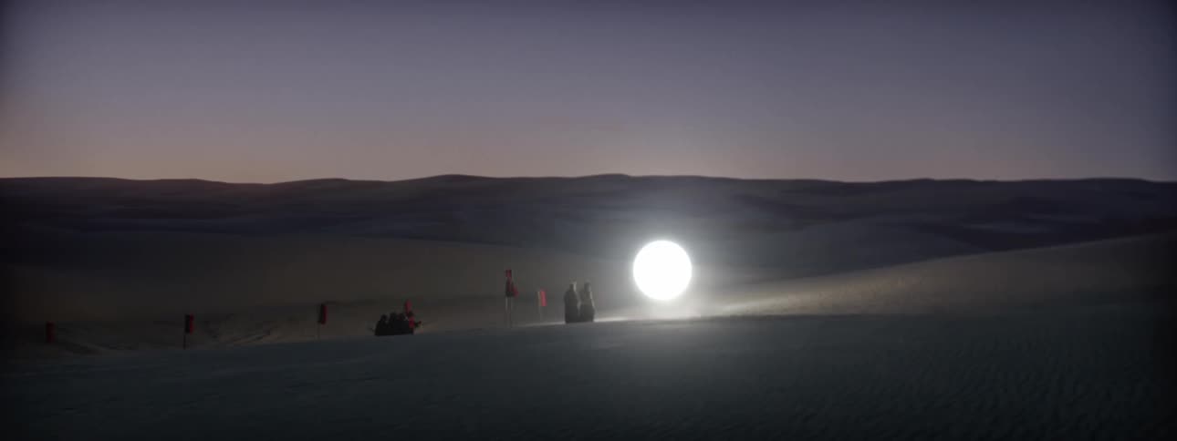 Two people stands next to an orb of light floating over the desert at sunset