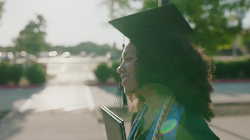 Young man and curlyhaired woman making a hand sign while wearing a graduation cap in an outdoor setting