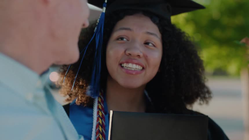Father next to his daughter who is wearing a graduation gown talking smilingly
