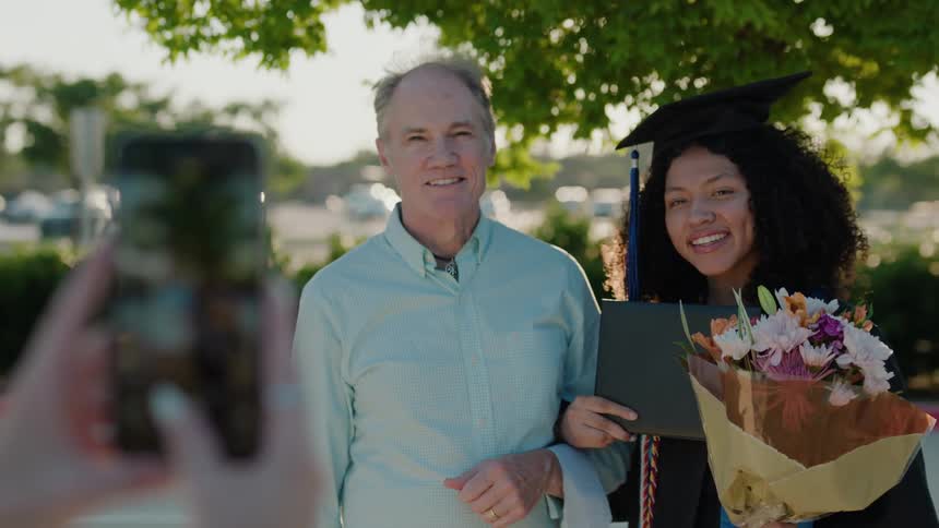 A white man and a biracial young woman holding her diploma pose for a photo
