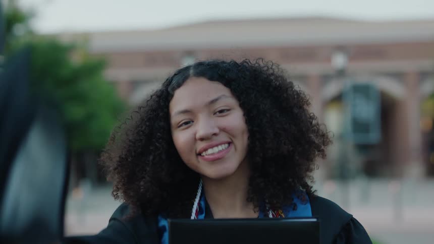 Woman tosses her graduation cap in the air in front of a building