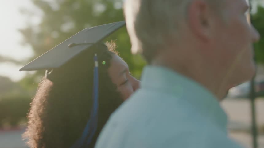 Father standing next to his daughter who is wearing a graduation gown with a feeling of pride