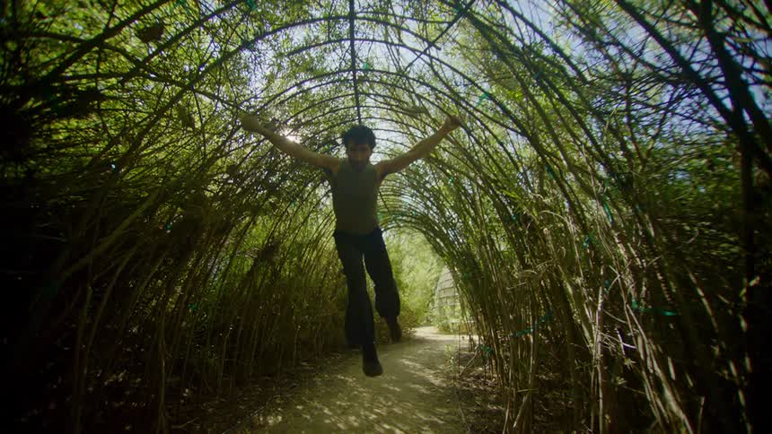 Man leaning on a bamboo arch with trees around him dancing