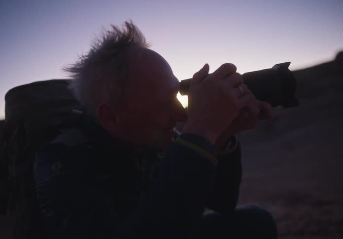 An elderly man is crouching and taking photos with a professional camera