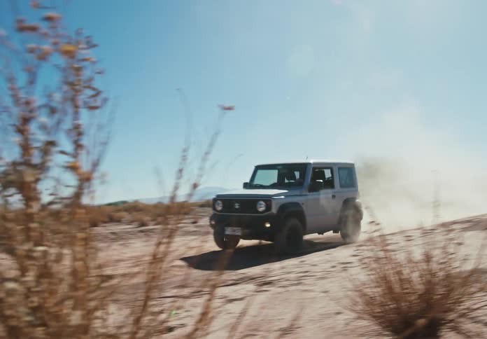A white suv drives along a dusty trail in the desert under a blue sky