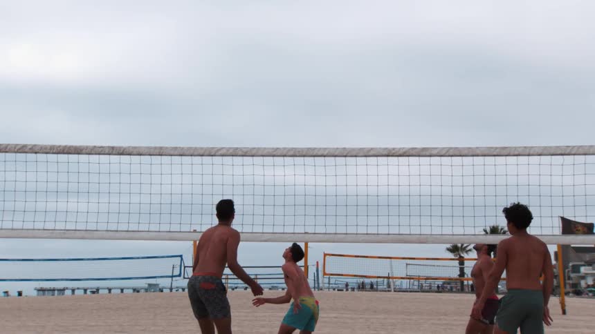 Slow motion of four guys playing beach volleyball on the sand