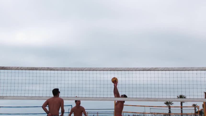 Two pairs of men playing volleyball on the beach sand