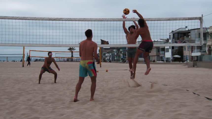 Men in pairs playing volleyball on the beach sand