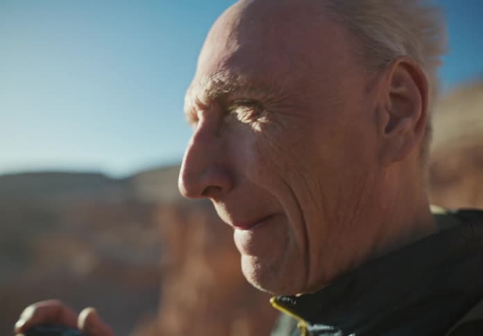 The face of an elderly man who is taking photos whith a camera and his gray hair is moving in the wind