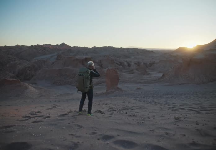 Man walking and taking photos in a natural environment with the sunset on the horizon and desert mountains