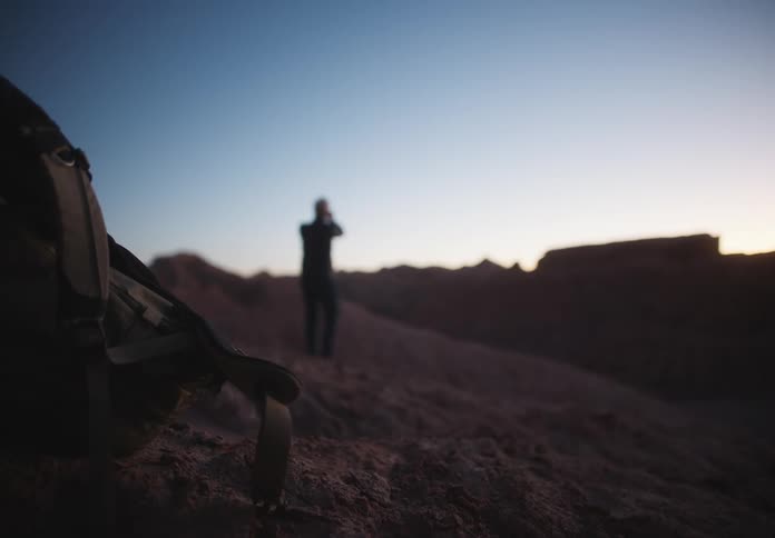 A person and a desert region taking photos of the sky and there is a backpack in front with which he walks to it later