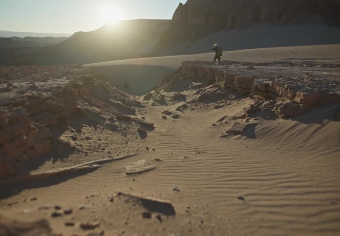 Person walking in a desert environment with sand and mountains