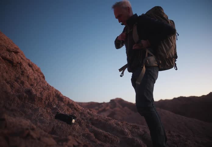 A photographer carrying a backpack in the barren mountains at dusk