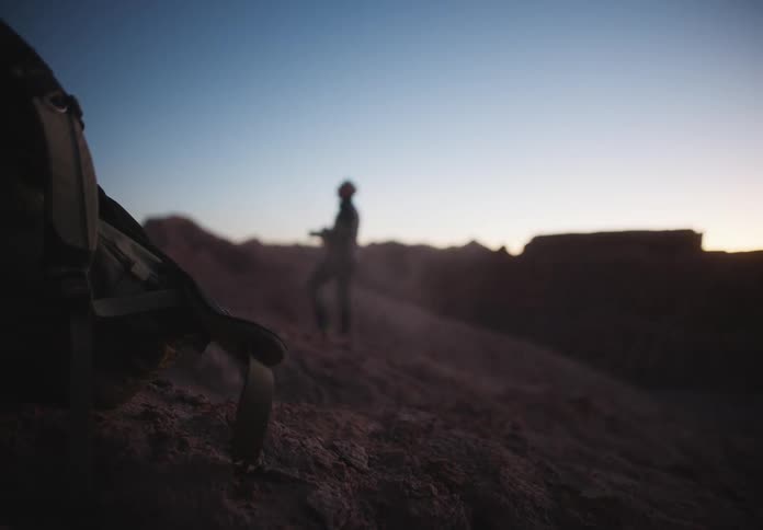 Backpacking in the foreground in a mountainous and desert natural environment with a man photographing in the background