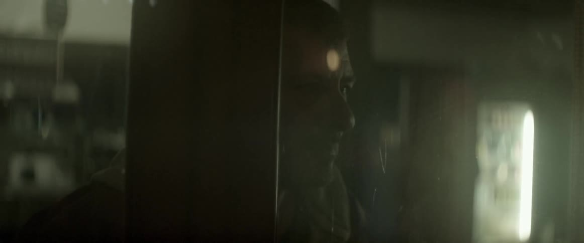 A man looks through a glass door as a person shines a flashlight in the background