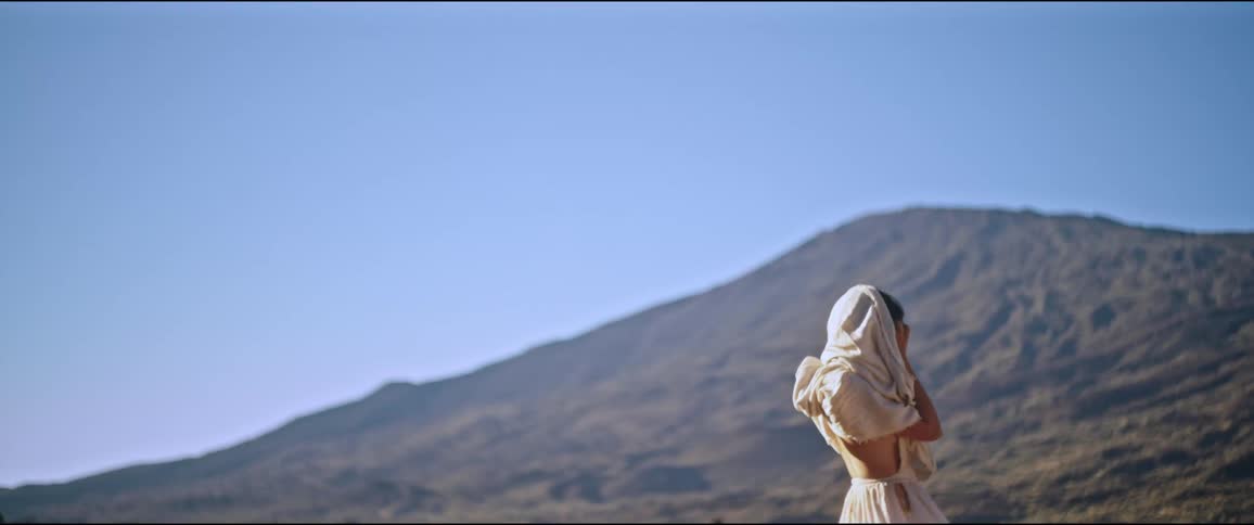 Woman with white scarf on her head while in a natural environment with a mountain in the background